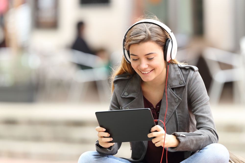 Menina aprende estudando através de um tablet e com fones de ouvido. As tecnologias tornaram mais fácil a propagação da educação digital.