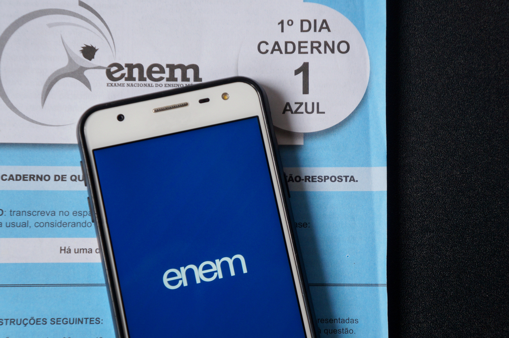 A imagem traz a foto de uma prova do ENEM da cor azul e por cima um celular aberto no aplicativo do ENEM. O objetivo da imagem é ilustrar o artigo sobre avaliações digitais já que existe a perspectiva de que o ENEM seja totalmente digital no futuro.