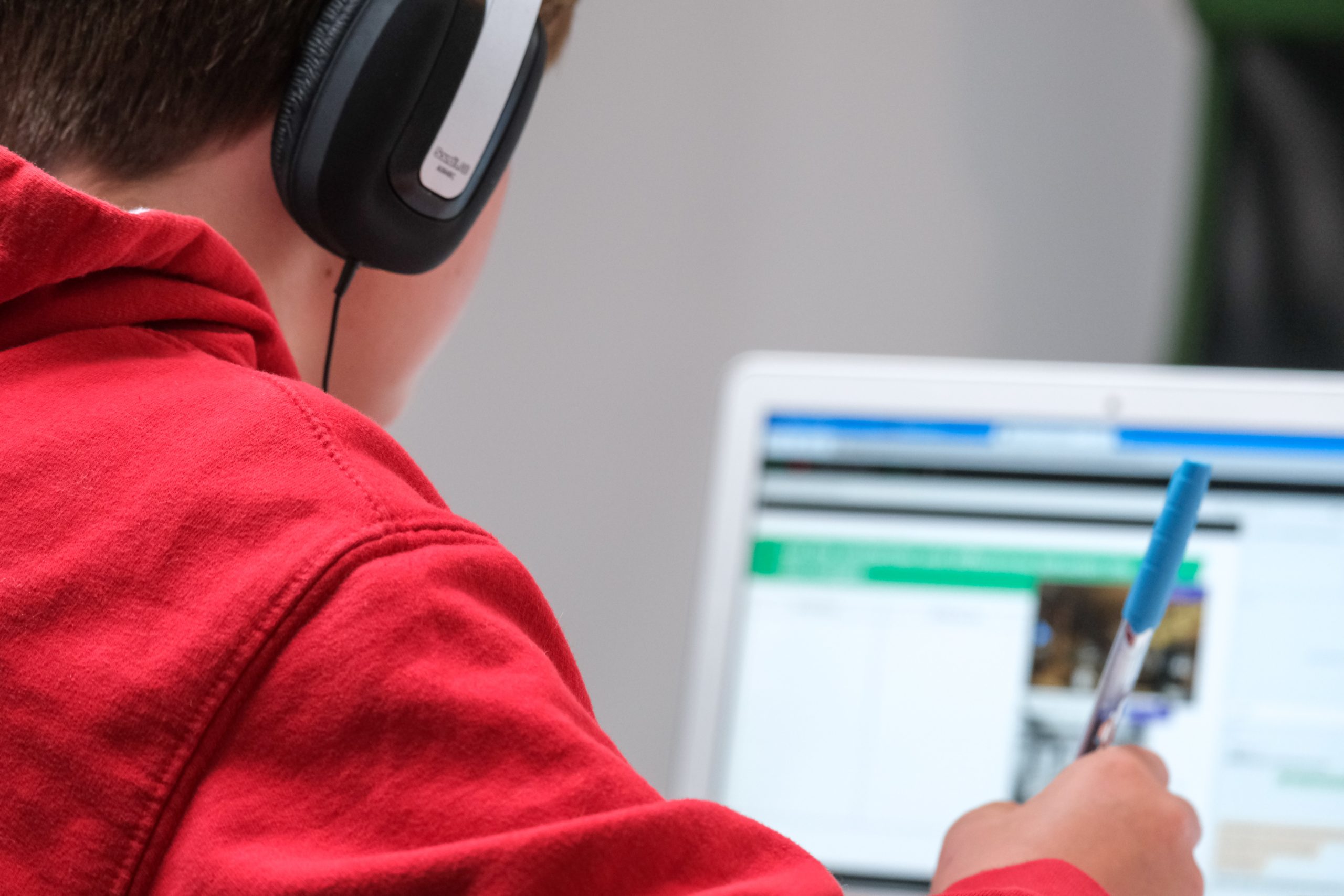 A imagem traz uma criança vestida de moletom vermelho estudando em frente ao computador. A imagem tem como objetivo ilustrar o artigo sobre alfabetização digital.