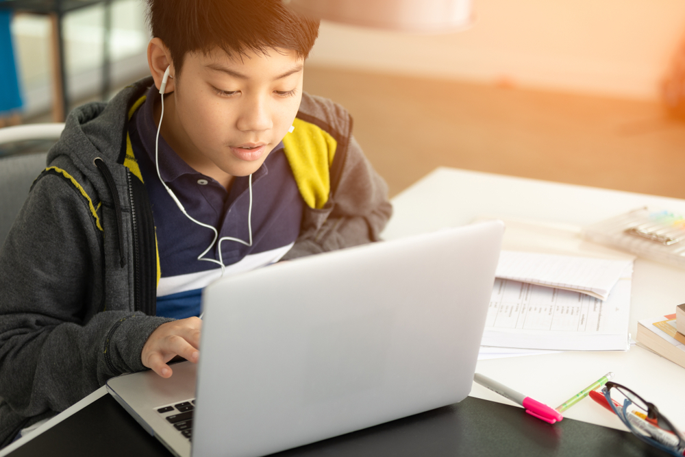A imagem traz um garoto que tem por volta de 11 anos estudando na frente de um notebook. Ele está rodeado de papeis e parece interessado no que ver. A imagem foi usada para ilustrar a mudança de segmento de ensino.